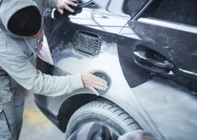 Mechanic worker repairman sanding polishing car body and preparing automobile for painting in workshop garage